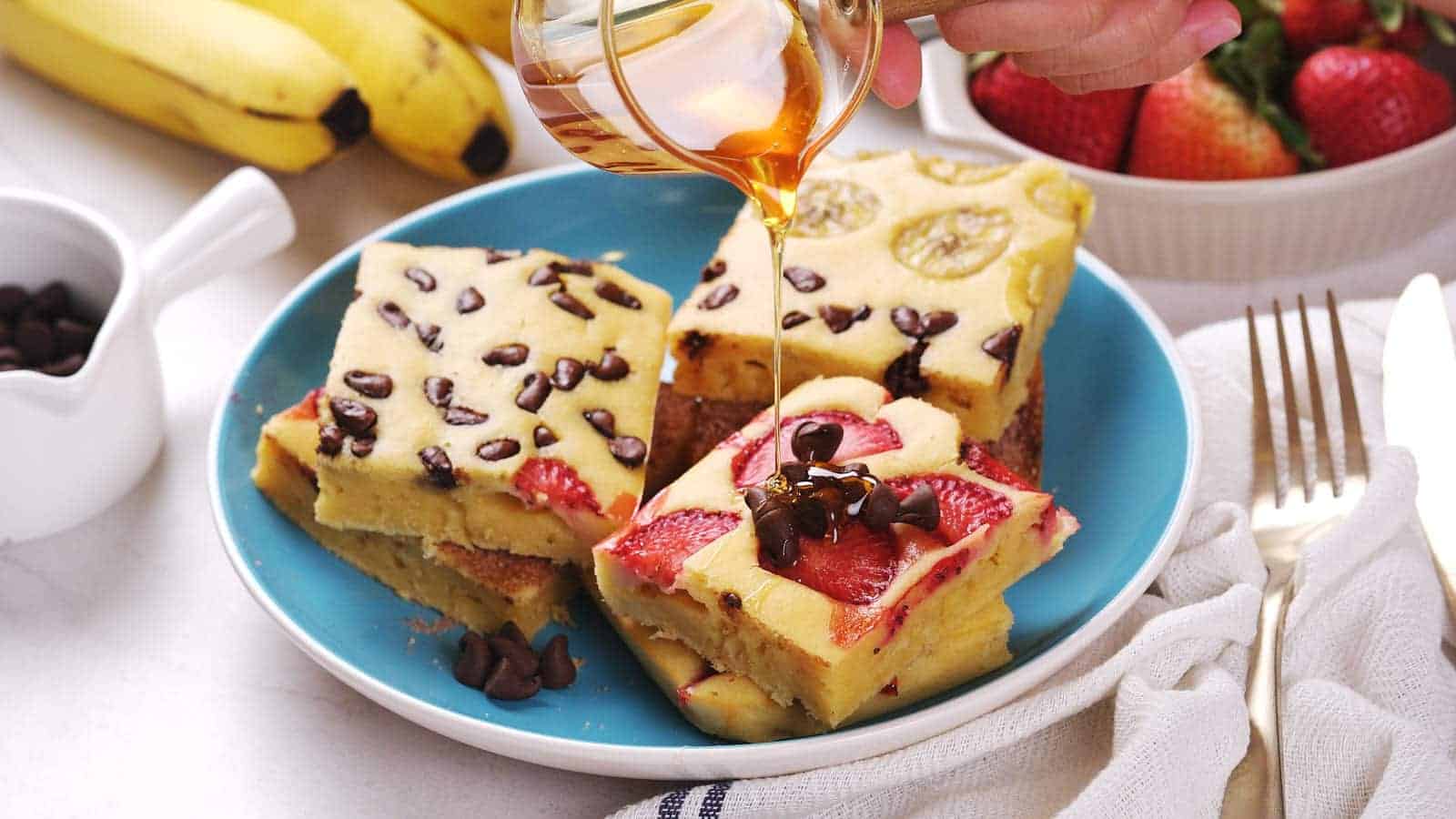 Three pieces of sheet pan pancakes topped with banana, strawberries, and chocolate chips on a blue plate.