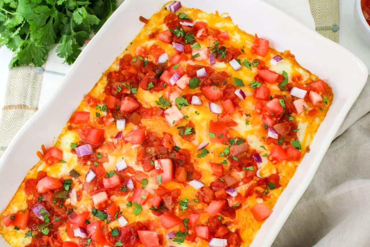 Casserole dish with melted cheese, diced tomatoes, onions, and chopped cilantro on top, with a side bowl of salsa and cilantro garnish nearby.