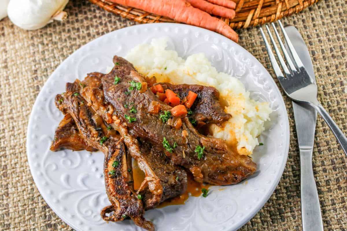Beer braised short ribs on a plate on top of a bed of mashed potatoes.