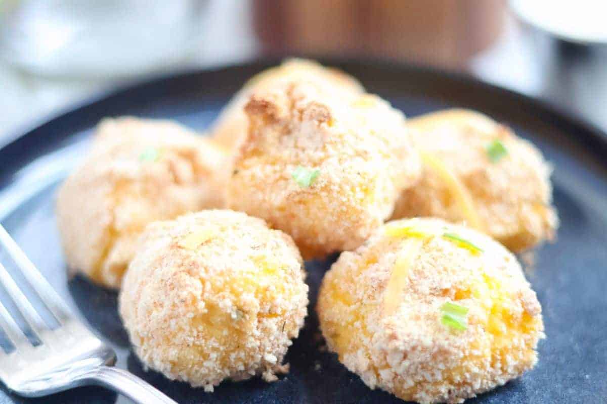 Five cheesy potato puffs on a plate with a fork.