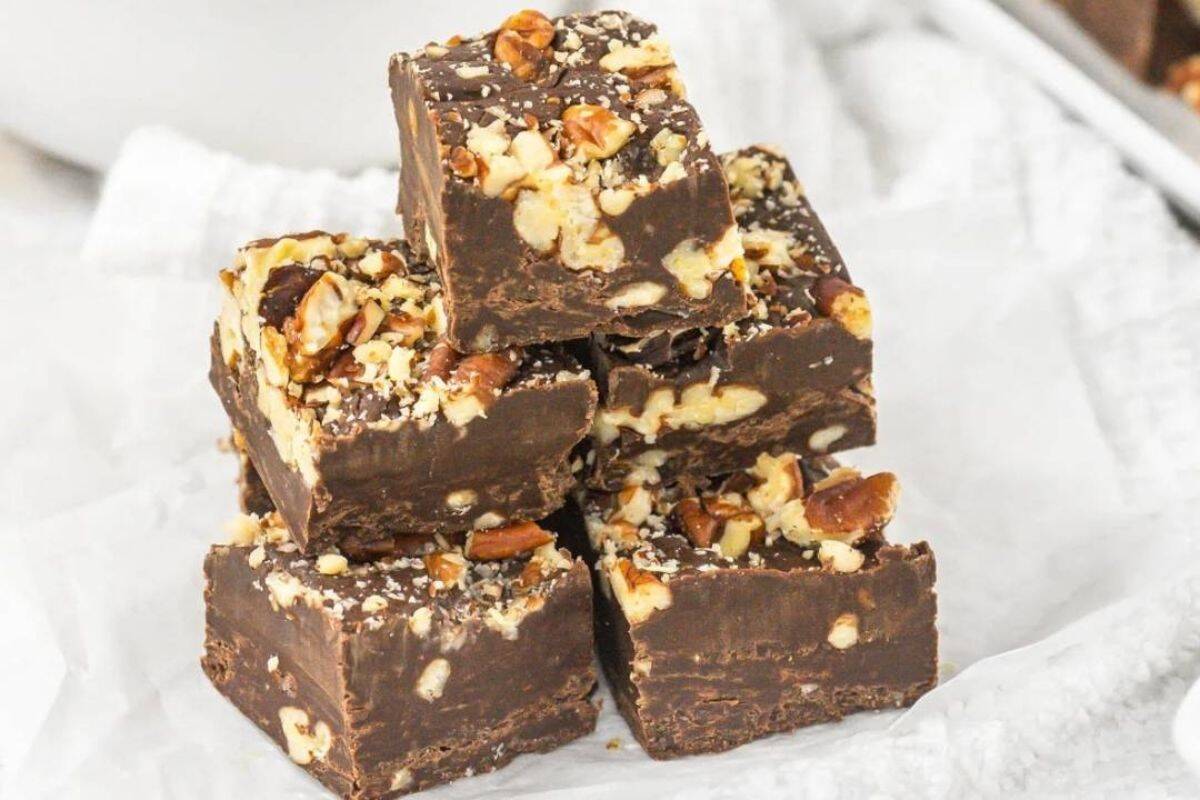 Five pieces of chocolate fudge with chopped nuts are stacked on white parchment paper.
