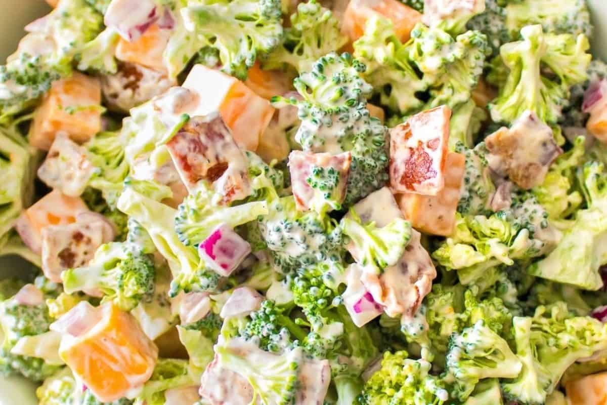 A creamy broccoli salad featuring tender florets, diced cheddar, red onions, and crispy bacon pieces, all coated in a luscious dressing.