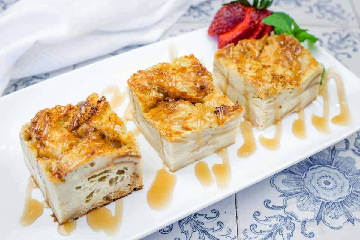 Three square pieces of Bourbon Croissant Bread Pudding with caramel drizzle are served on a white rectangular plate.