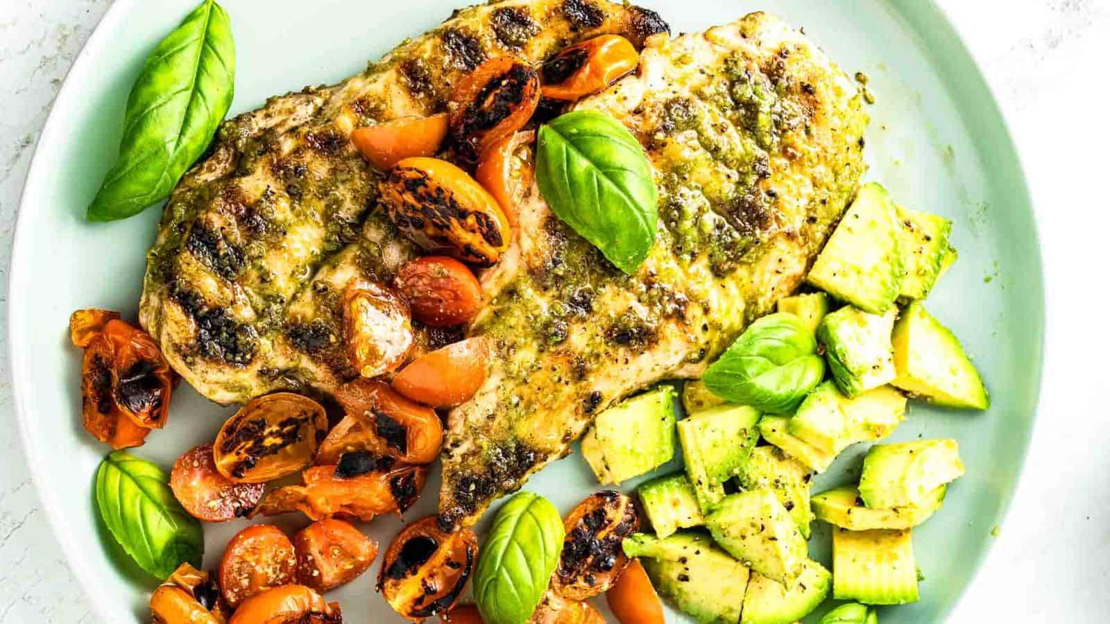 Plate of basil pesto chicken with grilled tomatoes and avocado slices.