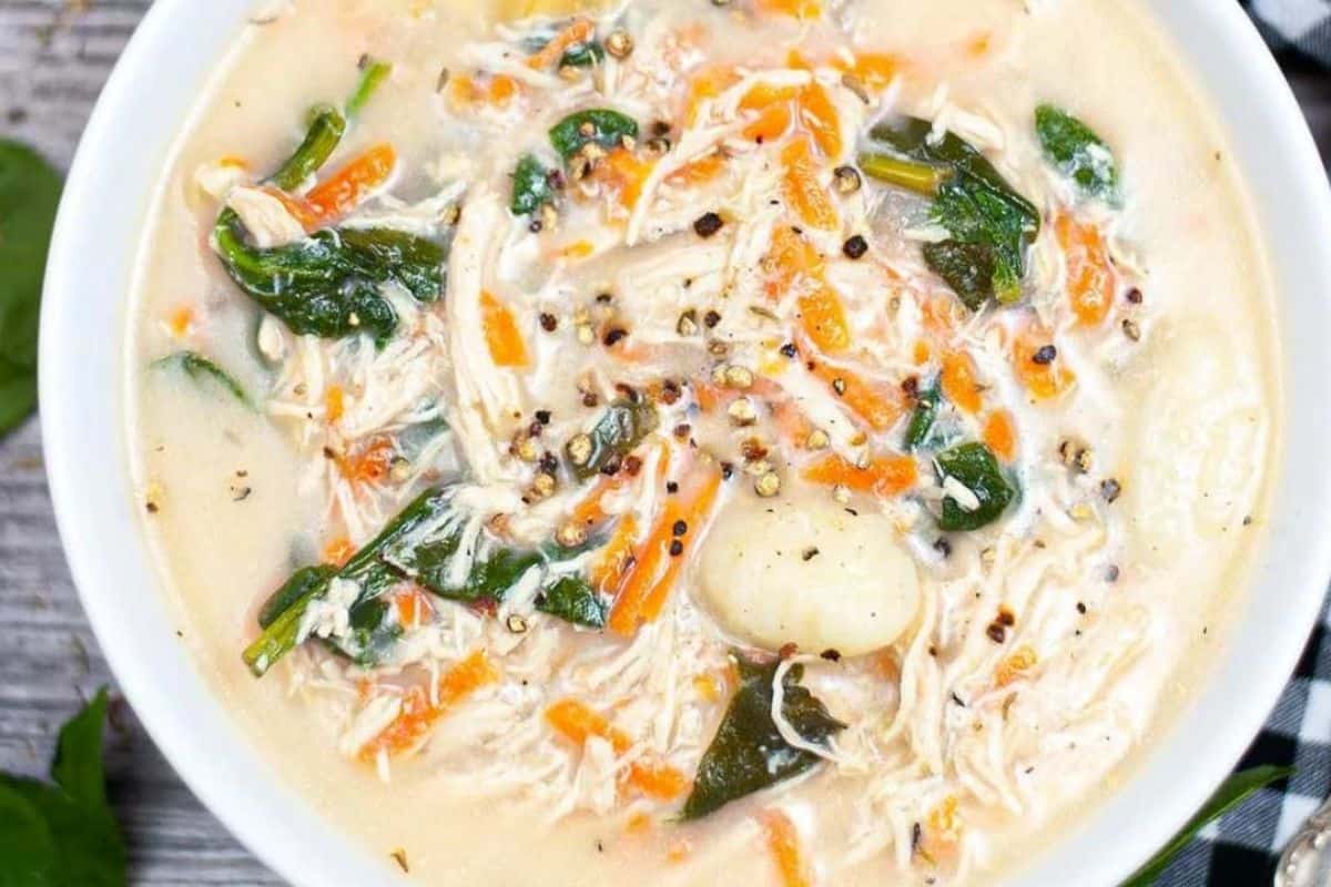A bowl of creamy chicken and gnocchi soup with shredded chicken, spinach, carrots, and black pepper.