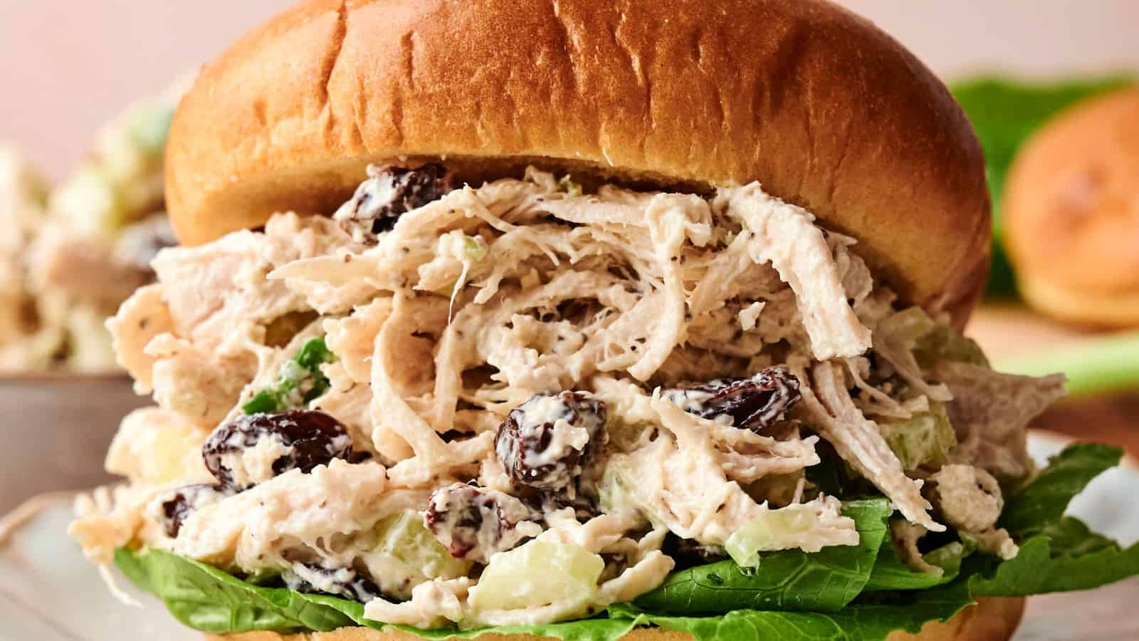 A shredded chicken salad sandwich with lettuce, raisins, and a creamy dressing served in a brioche bun.