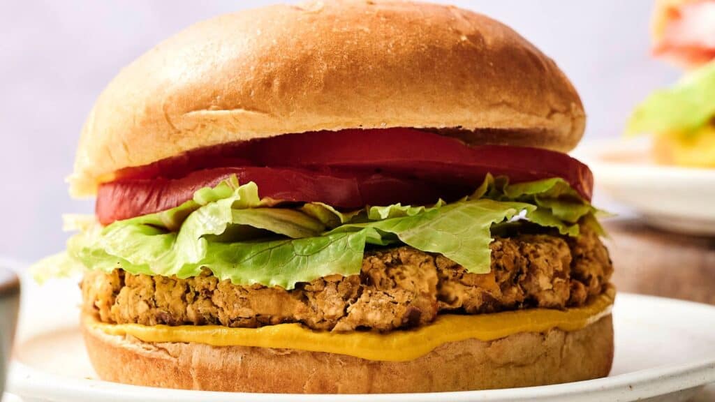 A veggie burger with lettuce, tomato slices, and mustard in a sandwich bun, served on a white plate.