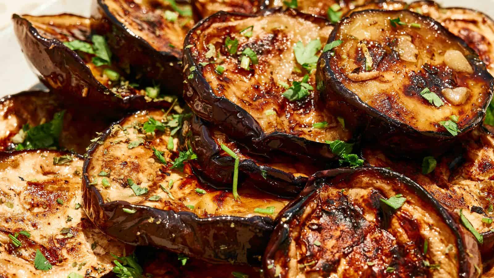 Close-up of grilled eggplant slices garnished with chopped herbs and a glossy glaze.