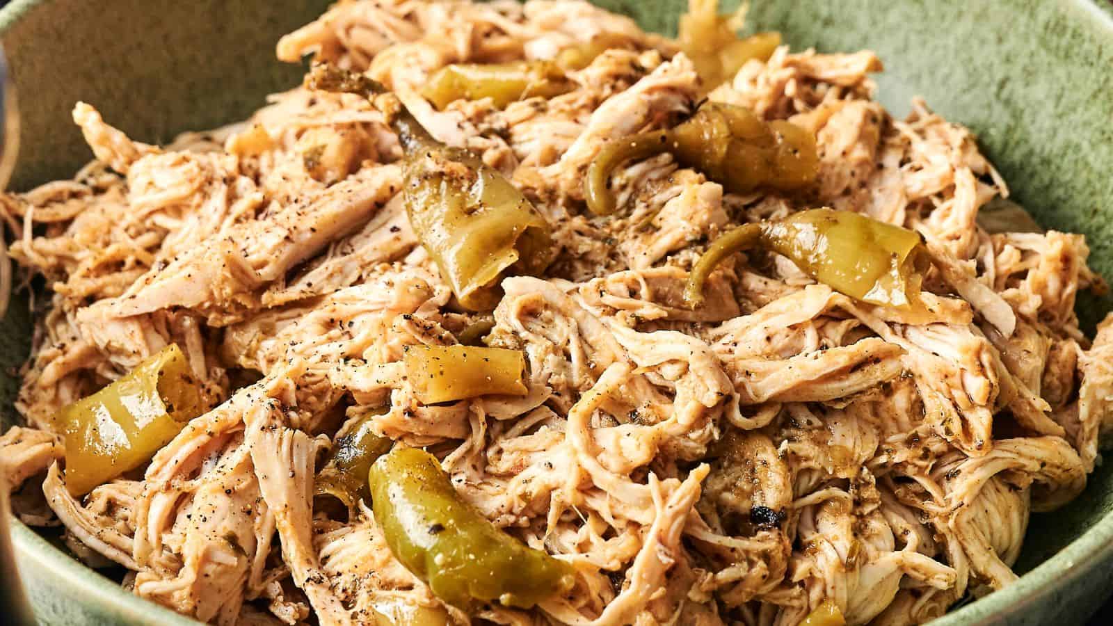 Shredded chicken mixed with sliced green peppers and seasoning in a green bowl.