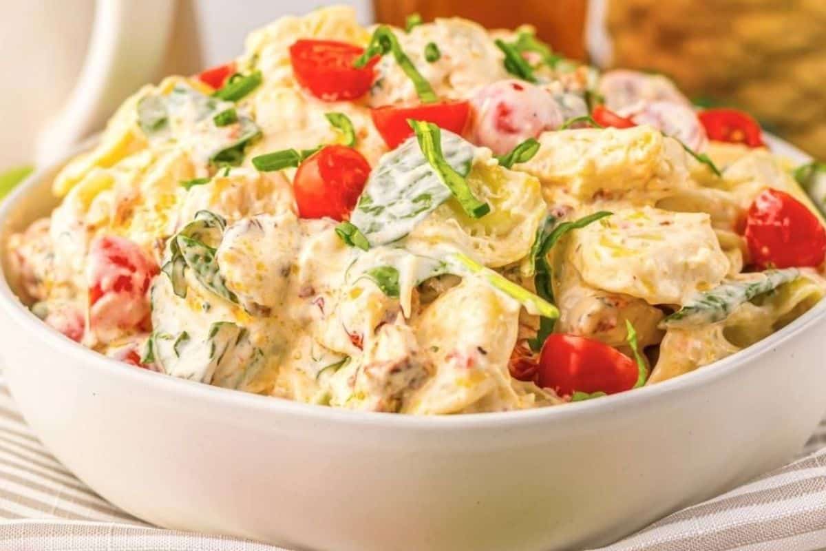 A white bowl filled with creamy pasta salad, mixed with chopped spinach, cherry tomatoes, and a creamy dressing.