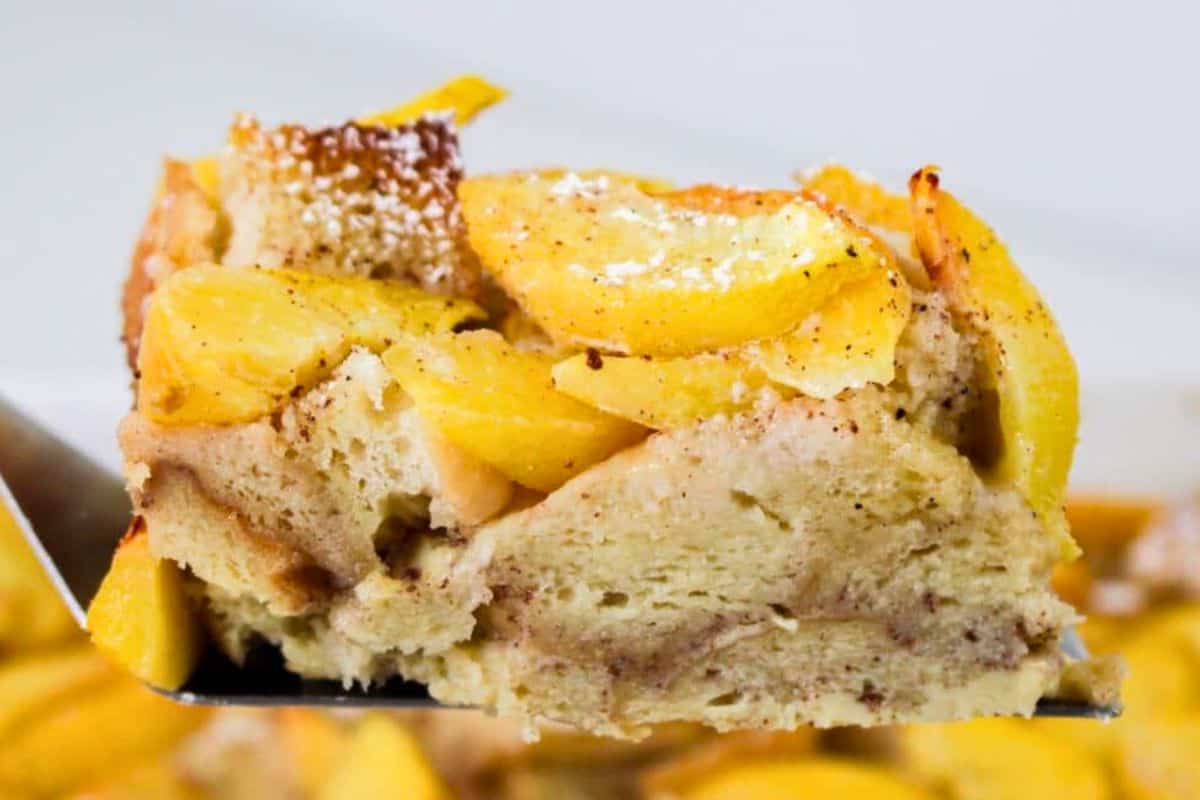 Slice of peach cobbler french toast held in the air on a spatula.