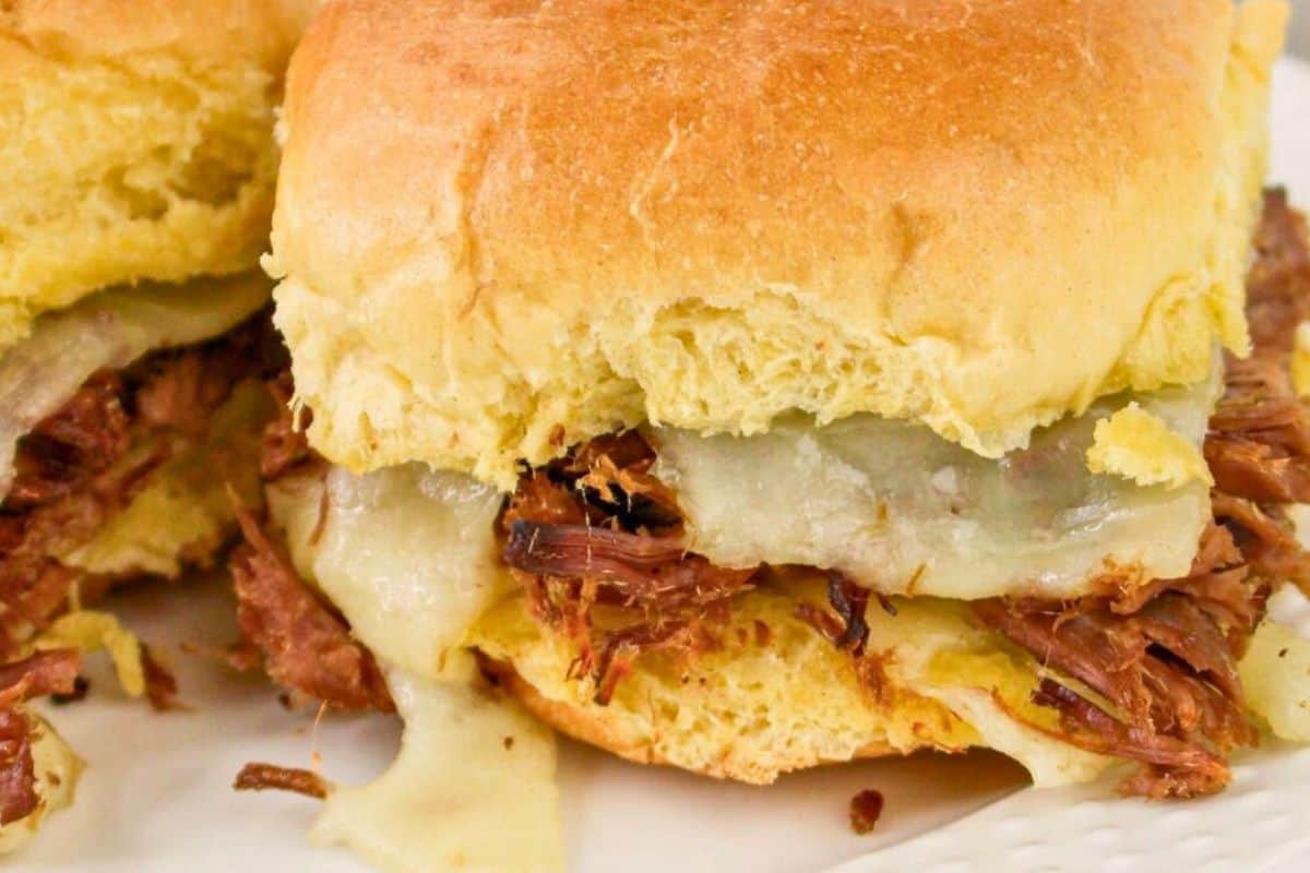 Close-up of a shredded beef and melted cheese sandwich on a soft, golden-brown bun.