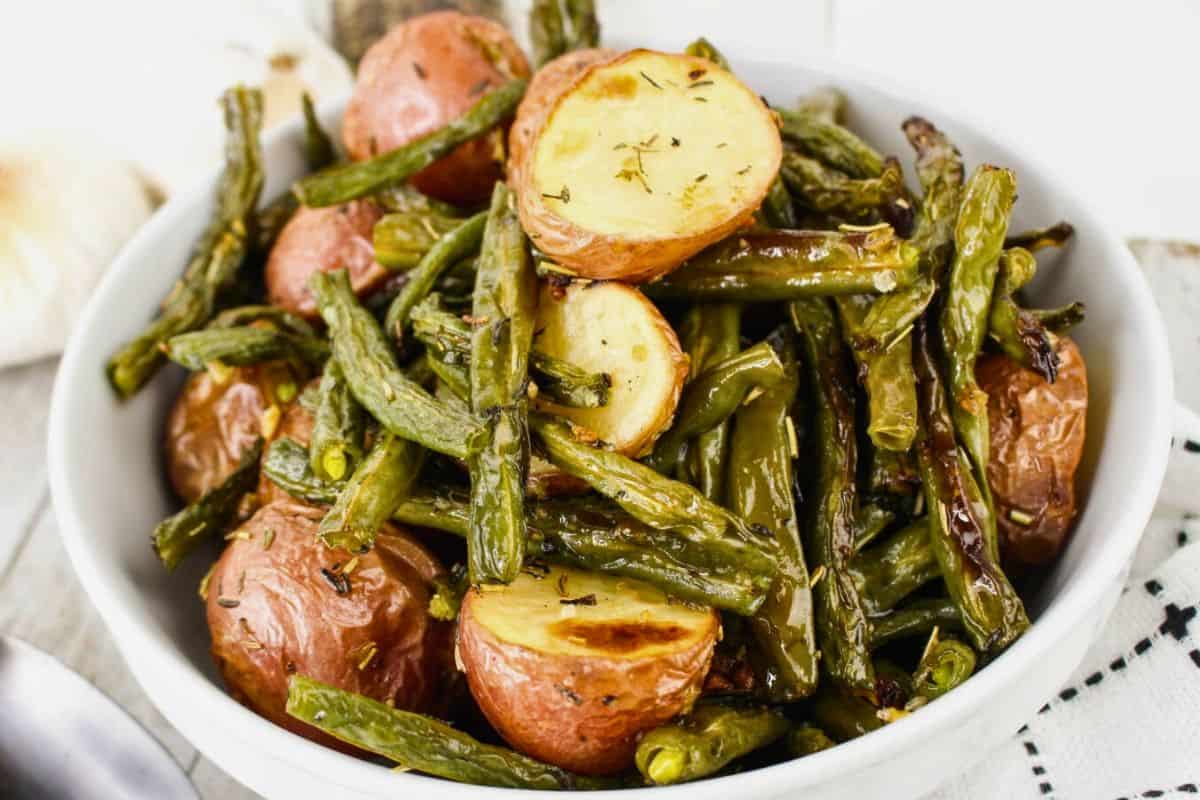 A bowl of roasted red potatoes and green beans seasoned with herbs.