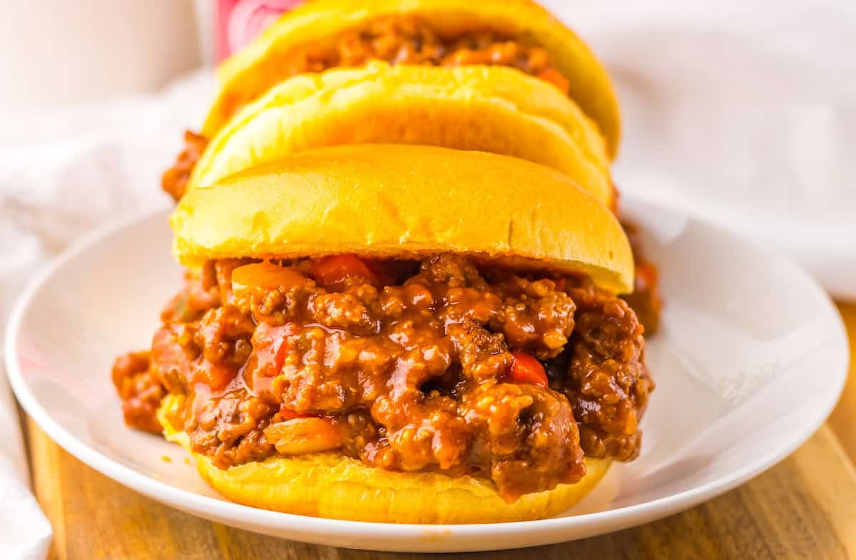 Three sloppy joe sandwiches filled with ground meat and sauce are placed on a white plate.
