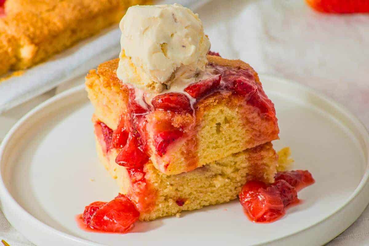 Two pieces of yellow cake topped with strawberry sauce and a scoop of vanilla ice cream on a white plate.