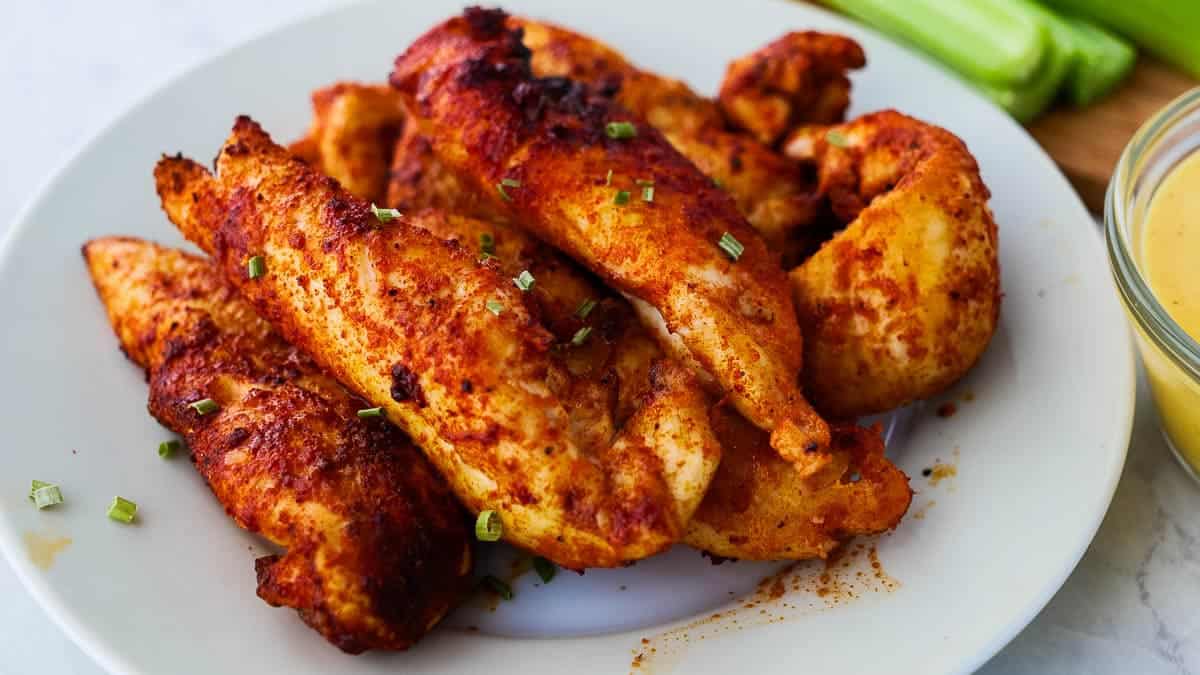 A plate of seasoned, cooked chicken tenders garnished with chopped green herbs.