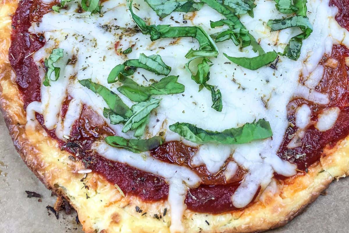 Cheese pizza topped with tomato sauce, melted cheese, and fresh basil on a parchment paper background.