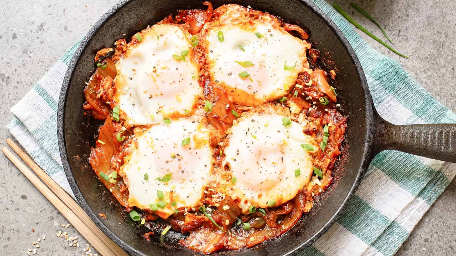 A hand dips bread into a skillet of shakshuka, featuring poached eggs, tomato sauce, and garnished with chopped green onions.