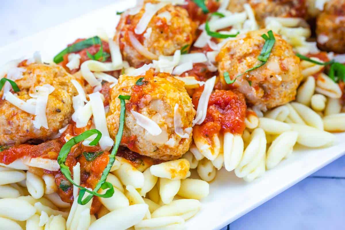 A plate of pasta topped with Chicken Parm meatballs, tomato sauce, shredded cheese, and fresh basil.
