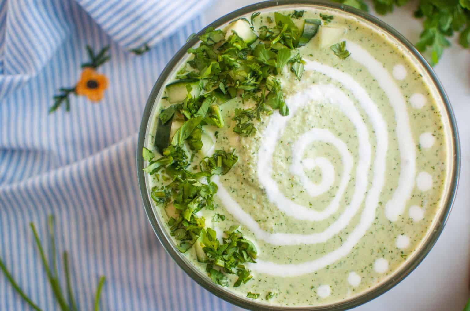 A bowl of Low-Carb Cool & Creamy Cucumber Gazpacho on a blue and white striped cloth.