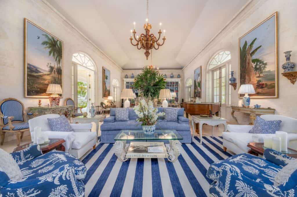 Elegant living room with blue and white striped rug, classic furniture, large paintings on the walls, chandelier, and a floral centerpiece on a glass coffee table&mdash;evoking the breezy charm of Barbados.