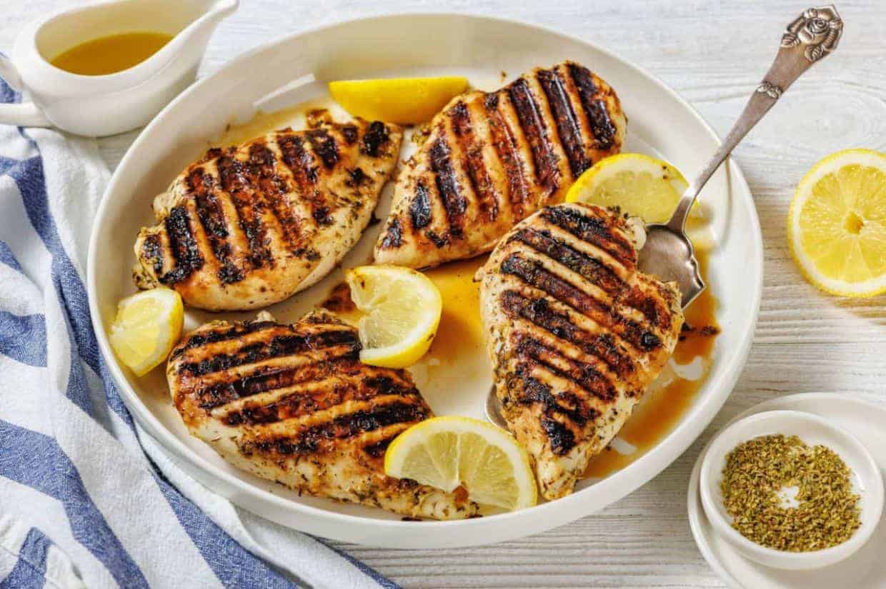 Grilled chicken breasts with charred grill marks, drizzled with sauce on a white plate, exuding a savory aroma.