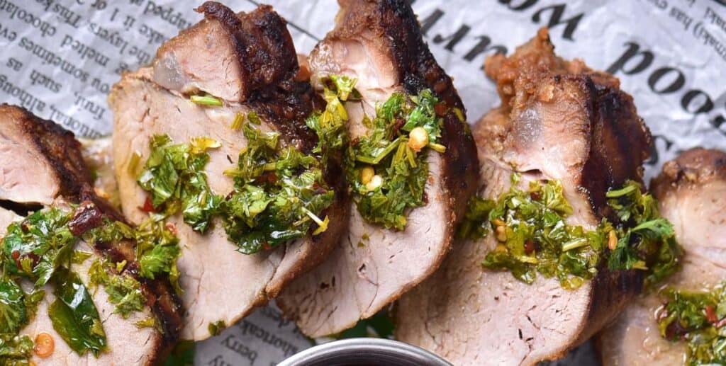 Sliced grilled meat topped with chopped herbs and spices, served on a sheet of printed paper.