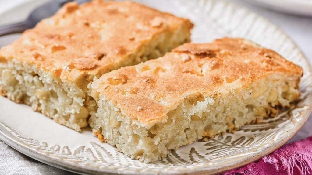 Two rectangular pieces of homemade cake with a golden, slightly crisp top are served on a decorative plate.