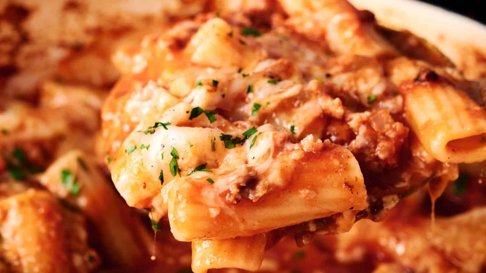 Close-up of baked ziti pasta with tomato sauce, ground meat, melted cheese, and sprinkled herbs.