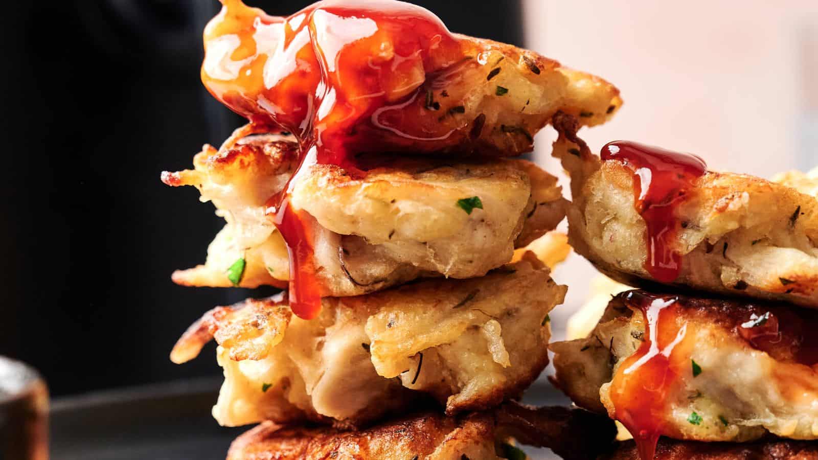 Stack of golden-brown fritters topped with a red sauce, showing crispy edges and bits of herbs.