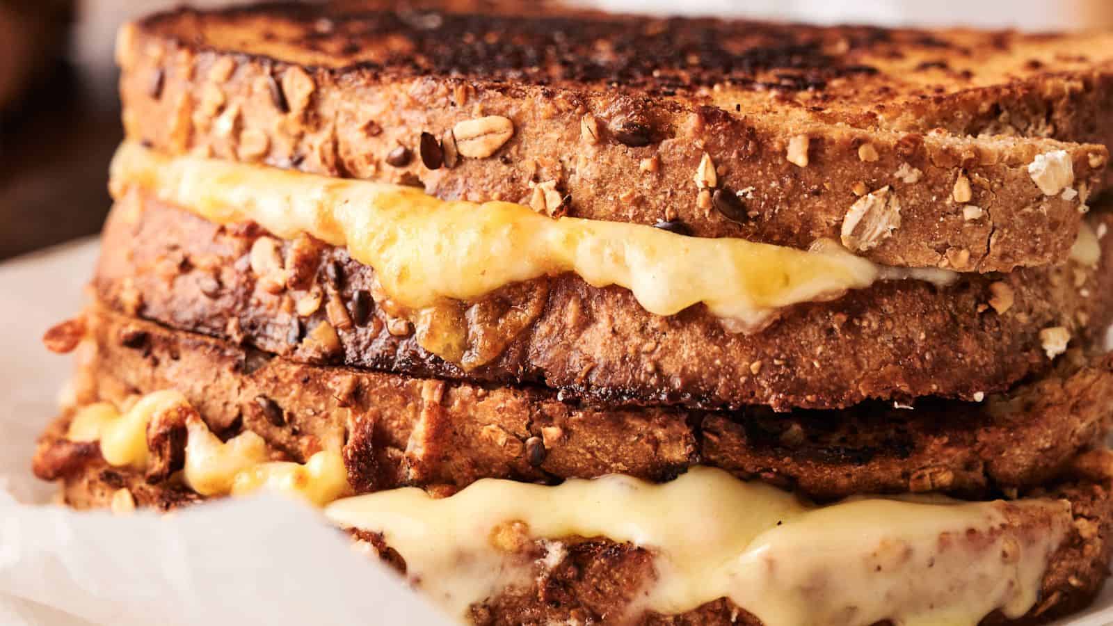 Close-up of two stacked grilled cheese sandwiches made with multigrain bread and melted cheese oozing out.