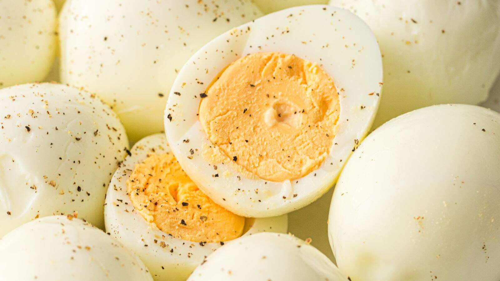 A close-up of several hard-boiled eggs, some whole and some halved, seasoned with ground black pepper.