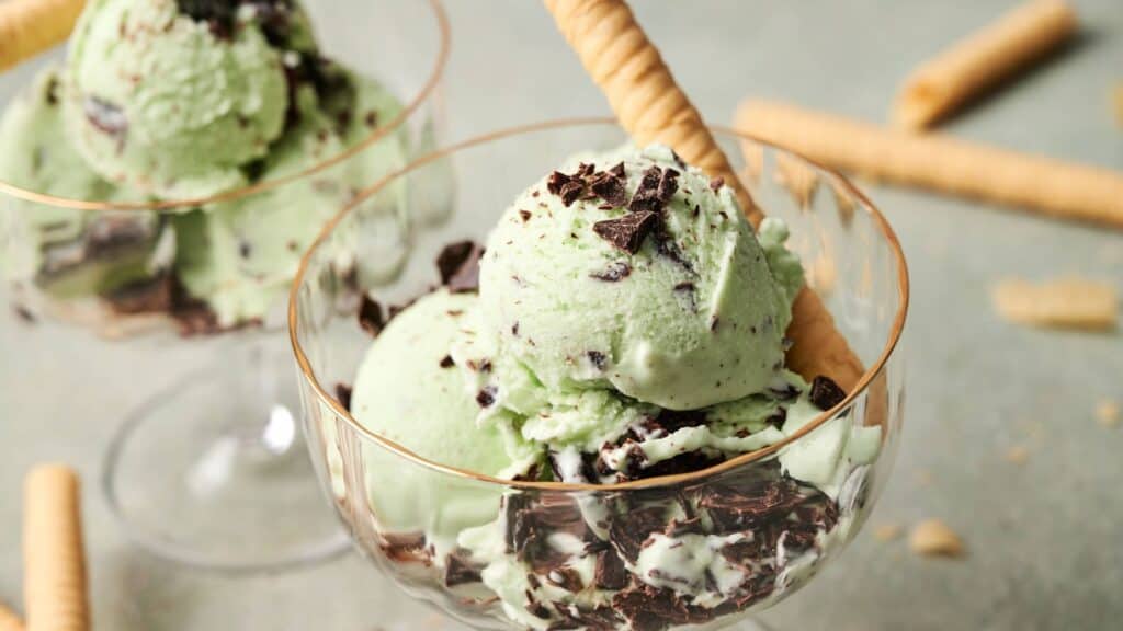 Two glass dessert cups filled with mint chocolate chip ice cream, chocolate chunks, and a rolled wafer cookie.