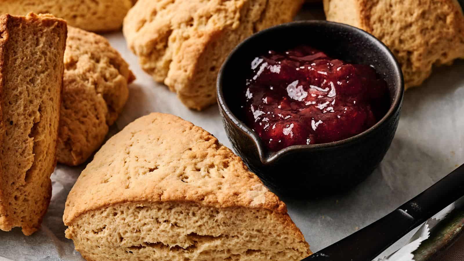 Triangular scones arranged on a tray with a small black bowl of red fruit jam placed in the center.