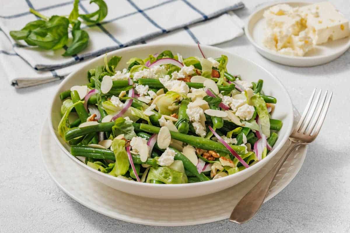 Fresh green bean salad with feta, red onion, and almond slices in a white bowl.