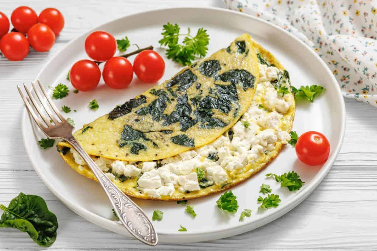 A spinach and feta omelette on a white plate, garnished with parsley and surrounded by cherry tomatoes.