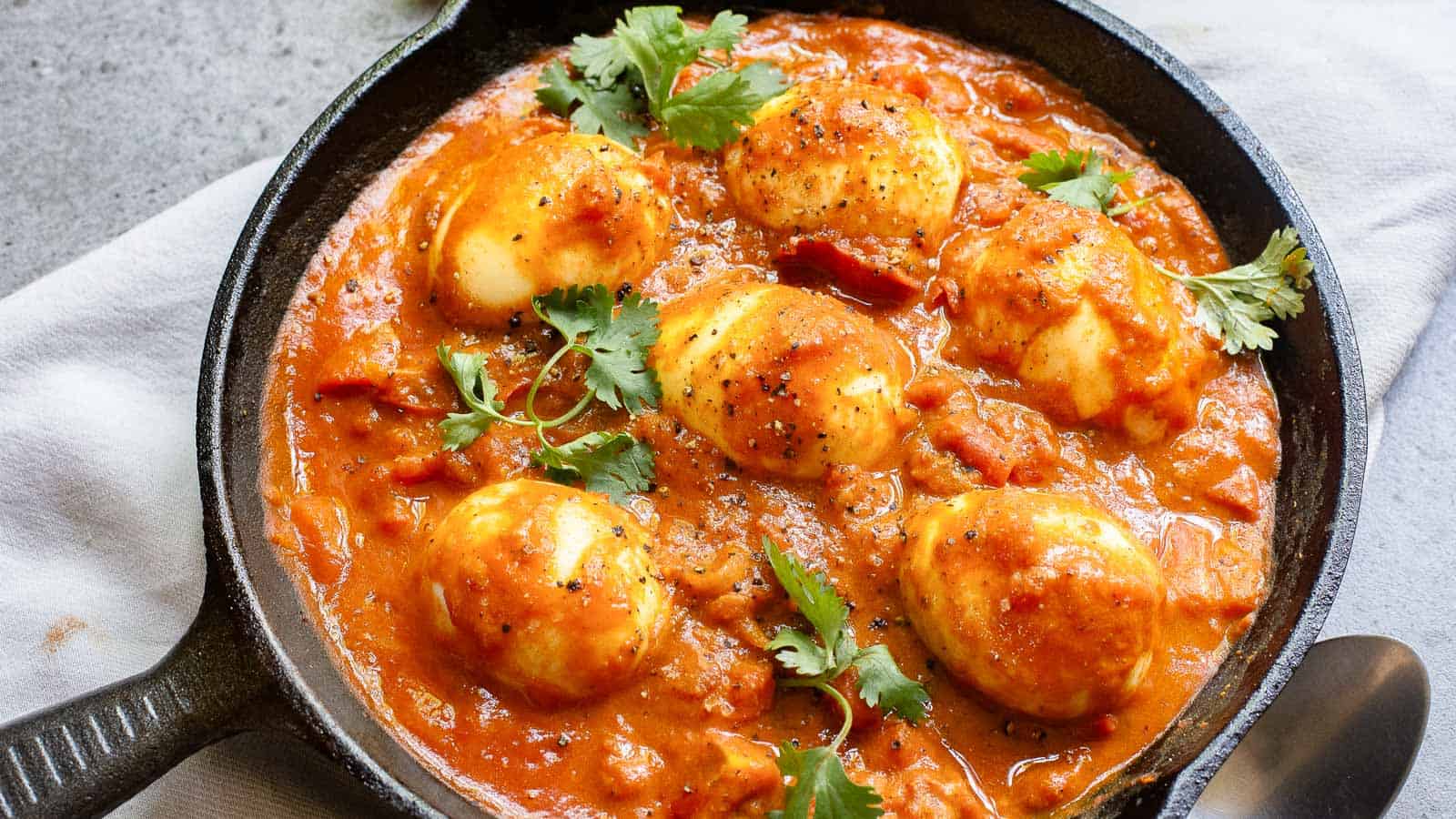 A skillet with eggs in a rich, spiced tomato sauce, garnished with fresh cilantro.
