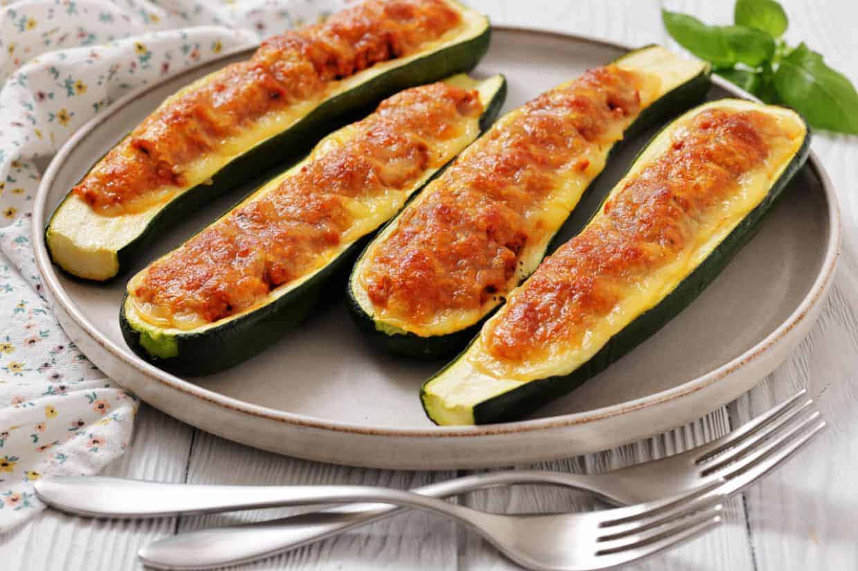 Four Baked Turkey Zucchini Boats are arranged on a round plate with two forks beside them.