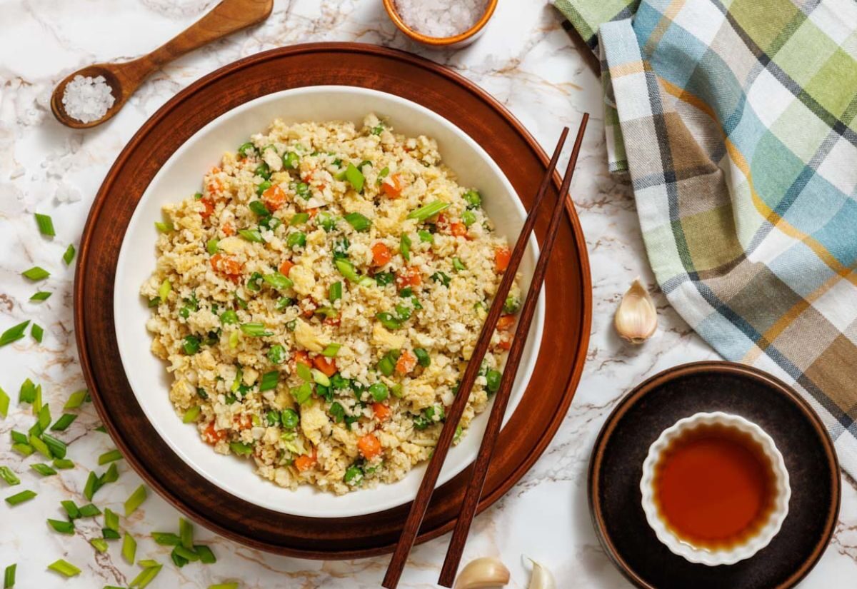 A bowl of cauliflower fried rice with chopped vegetables and scrambled eggs, garnished with green onions.
