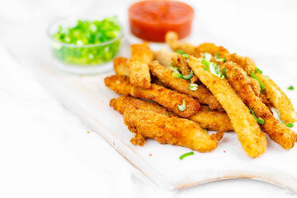 Chicken strips with chopped green onions on a white board.