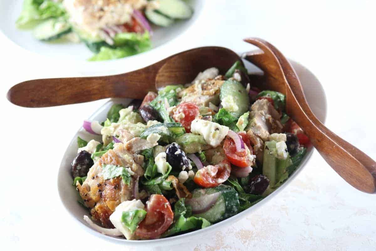Oval bowl filled with Chicken Mediterranean Salad Recipe with wooden salad servers on the side.