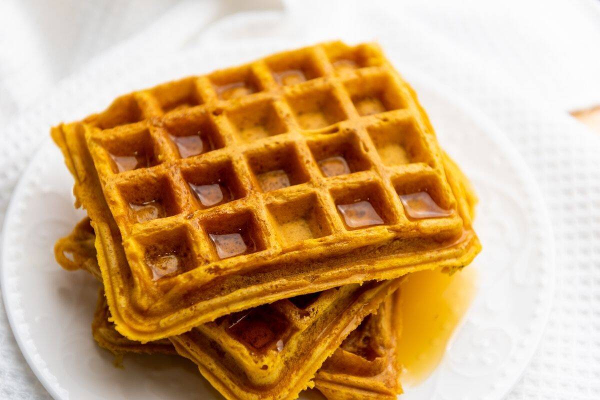 Two stacked square waffles with syrup on a white plate, set on a white textured surface.