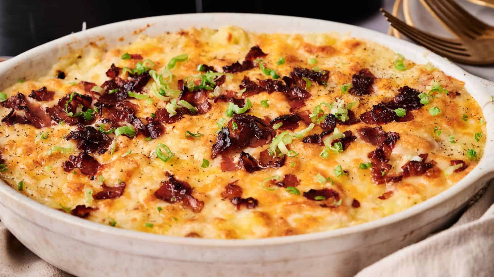 Baked casserole topped with melted cheese, crispy bacon pieces, and chopped green onions in a white dish.