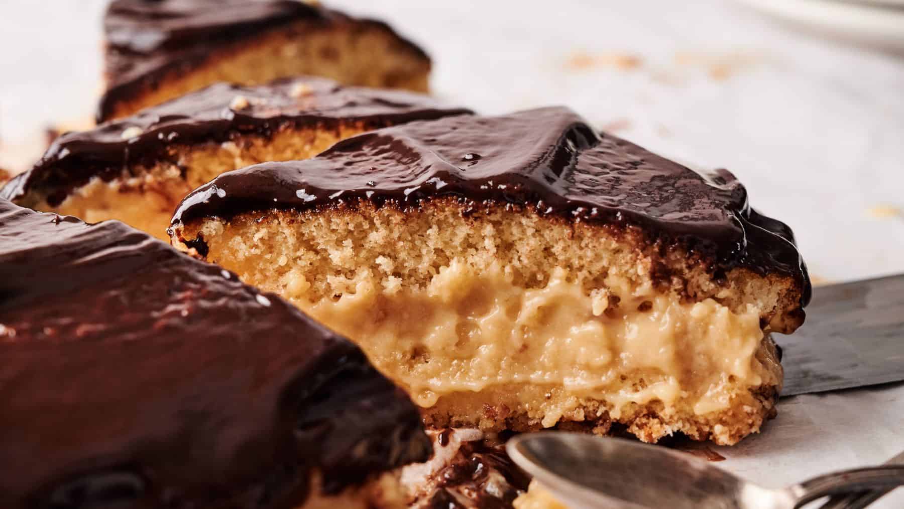 A close-up of sliced Boston cream pie showing yellow sponge cake layers filled with creamy custard and topped with glossy chocolate glaze.