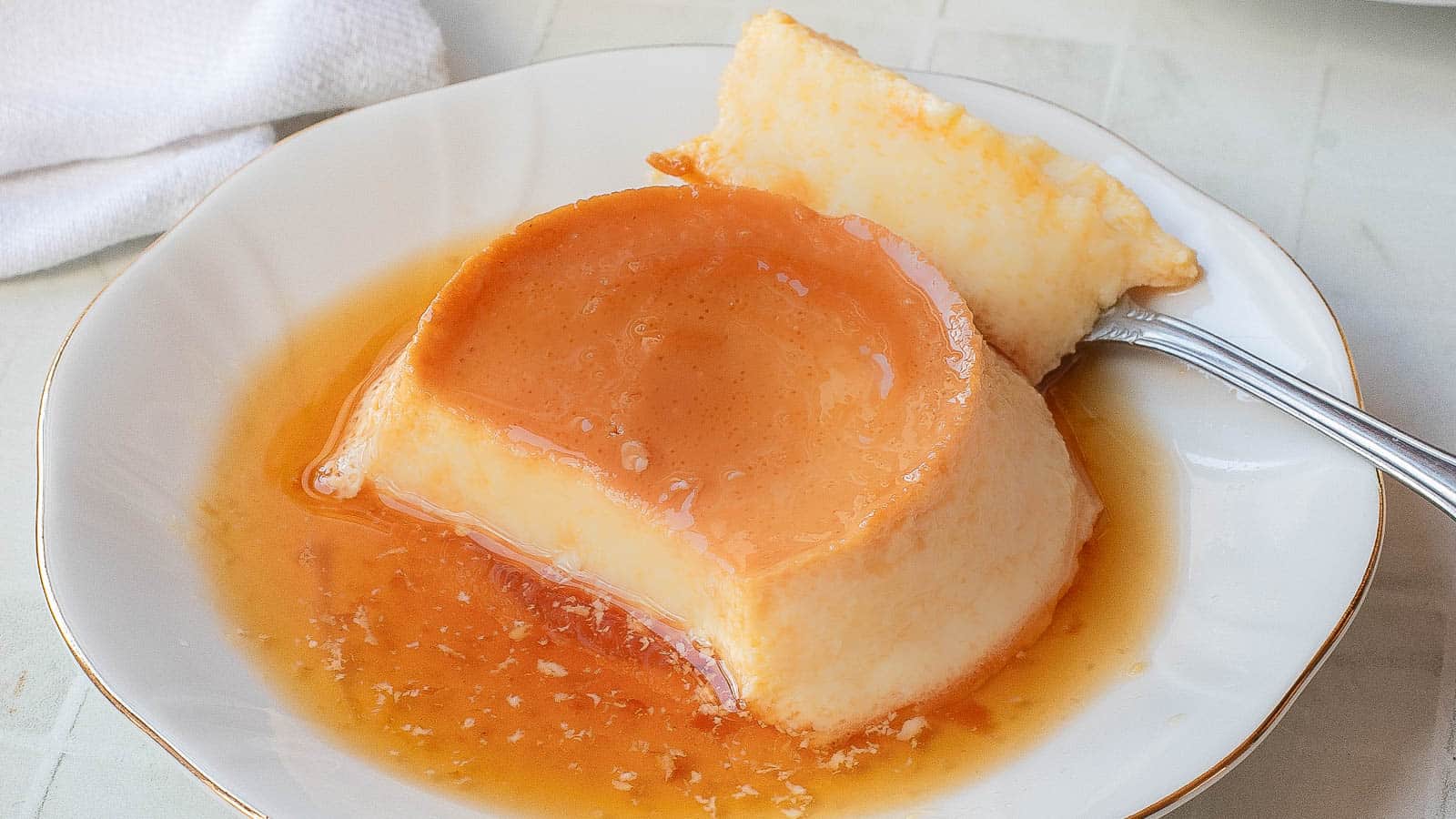 A plate with a serving of Vietnamese Egg Flan, topped with caramel sauce, with a fork holding a piece.