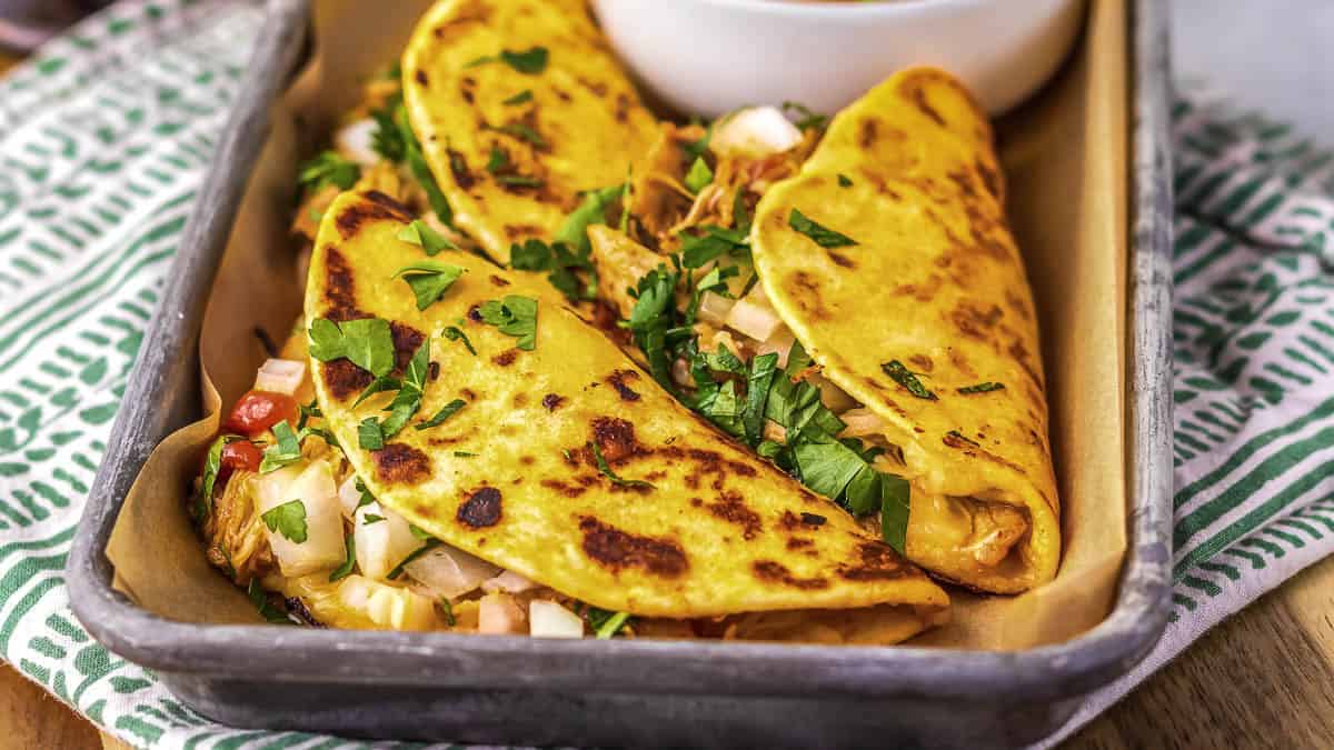 Two folded tacos filled with shredded meat, diced onions, and fresh cilantro are served in a tray on parchment paper.