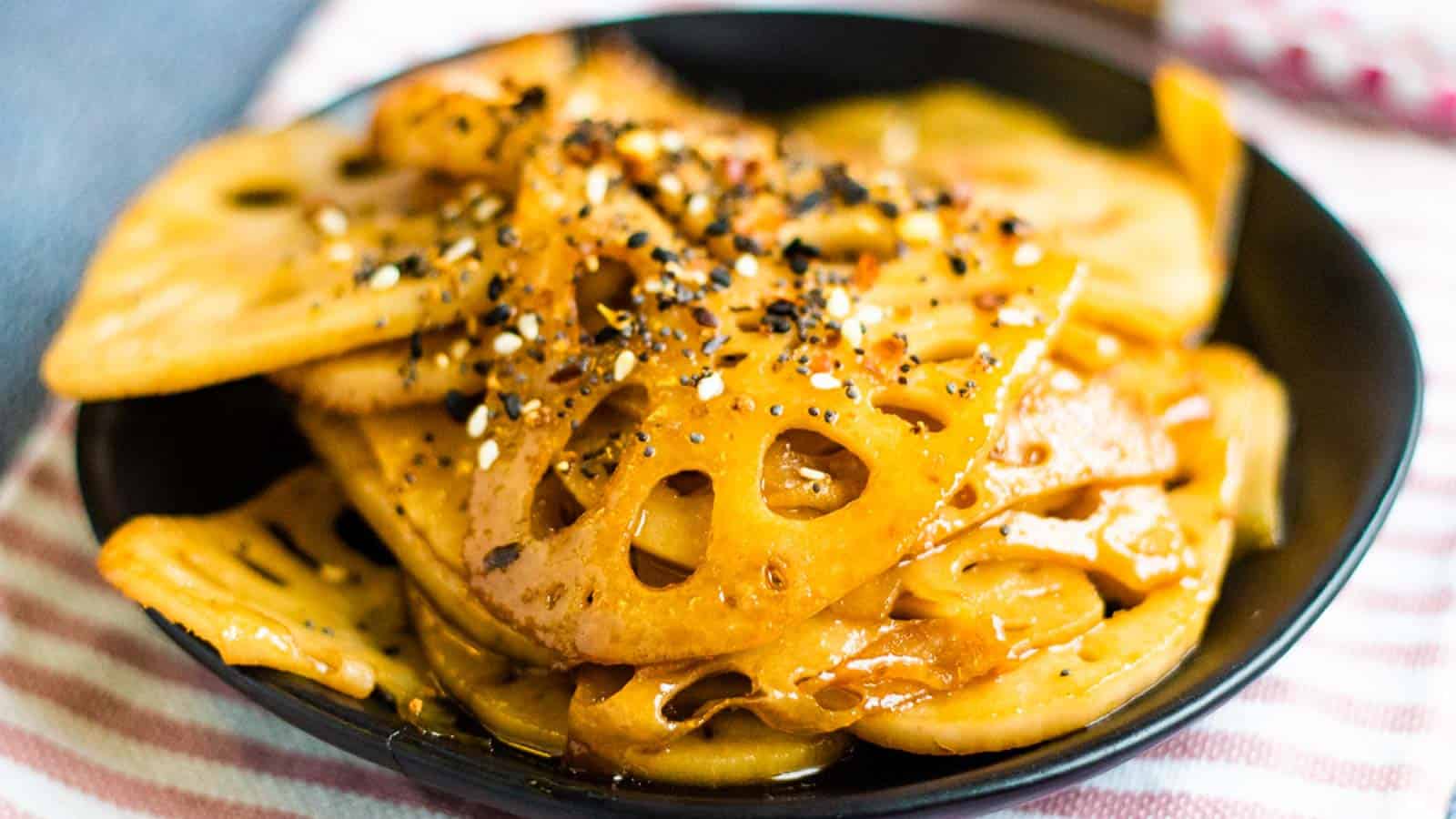A low-angled shot of a pile of stir-fried lotus root on a black plate.