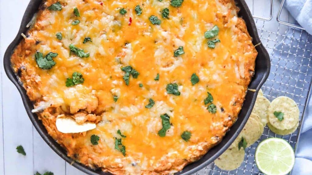 cheesy chicken enchilada dip in cast iron pan on blue background