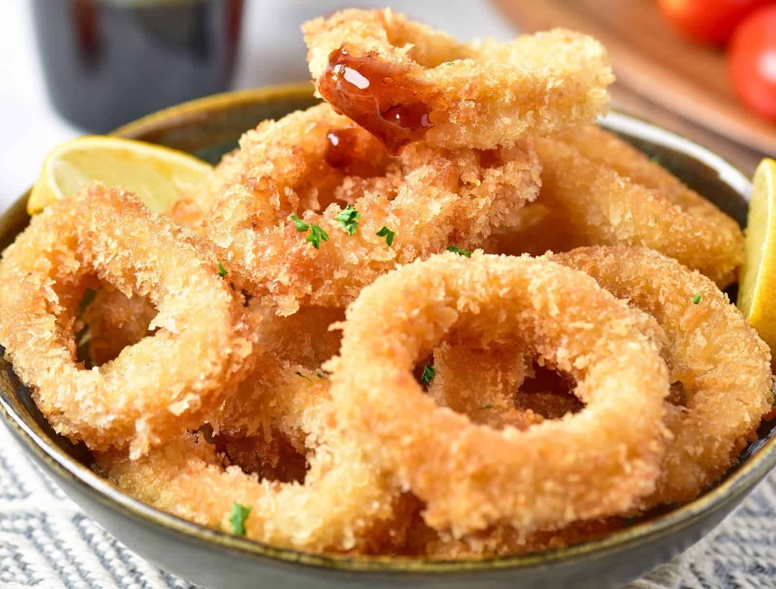 A bowl filled with golden, crispy fried calamari rings garnished with chopped parsley.