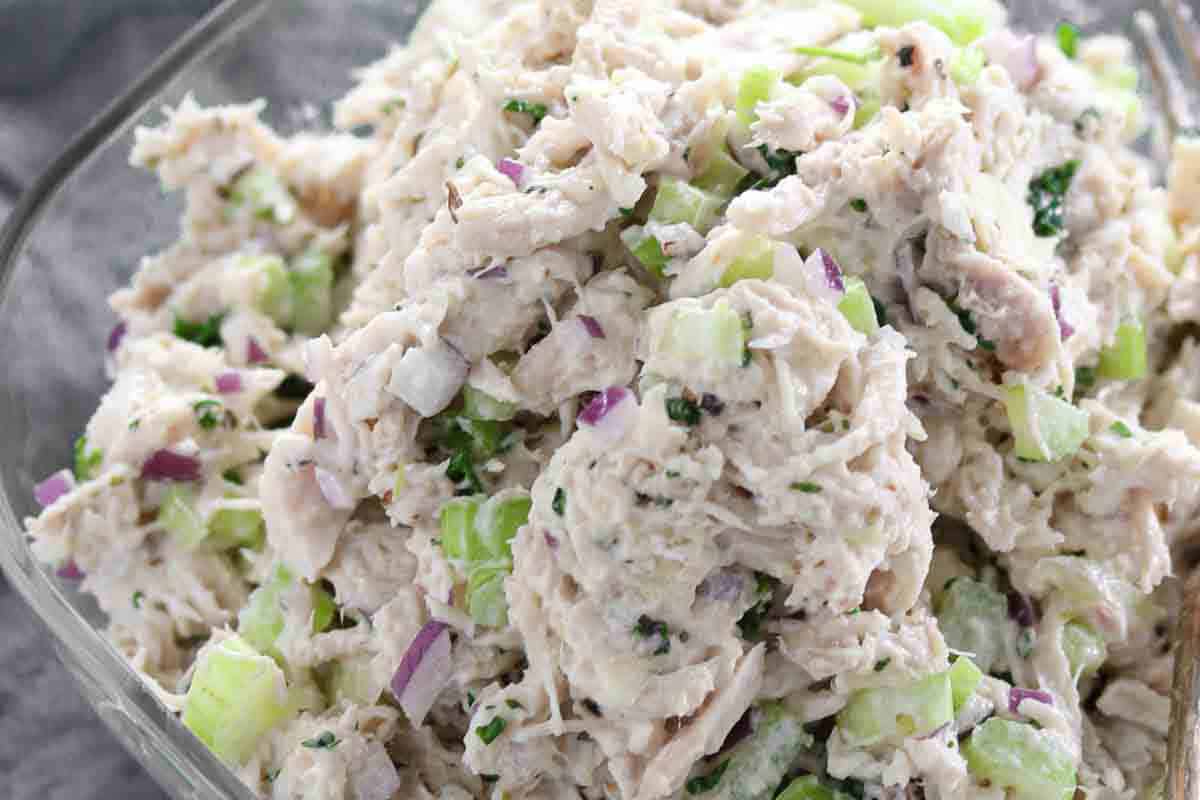 Close-up of chicken salad with chunks of chicken, diced celery, red onion, and herbs mixed with a creamy dressing.